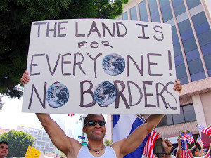 person holding a sign that says the land is for everyone! No borders!