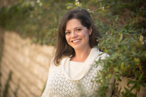Traci Brimhall Photograph of poet Traci Brimhall, a smiling woman with dark hair, wearing a white sweater