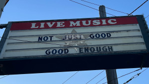 The outside marquee of a local bar which reads "LIVE MUSIC" & under it, the phrase "Not Just Good. Good Enough" with the Self Help Radio logo interposed on the sign.