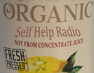 A manipulated juice label reads "Organic Self Help Radio Not From Concentrate Juice Fresh Pressed" with an image of a lemon at the bottom with the Self Help Radio logo stuck on it.