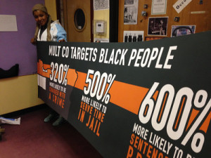 Teressa Raiford holds banner listing Black incarceration rates in Multnomah County
