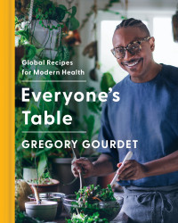 Book cover for Everyone's Table cookbook showing author/chef Gourdet tossing a salad in a plant filled kitchen.